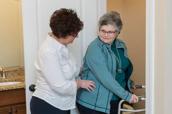 Lady with walker being assisted to the bathroom by Julie