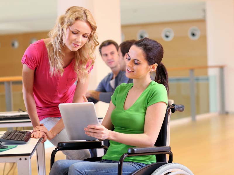 cheerful handicapped woman at work in wheelchair with coworkers